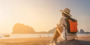 Woman traveling with backpack and looking over beach scene.