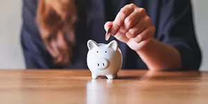 Woman adding a coin to a piggy bank.